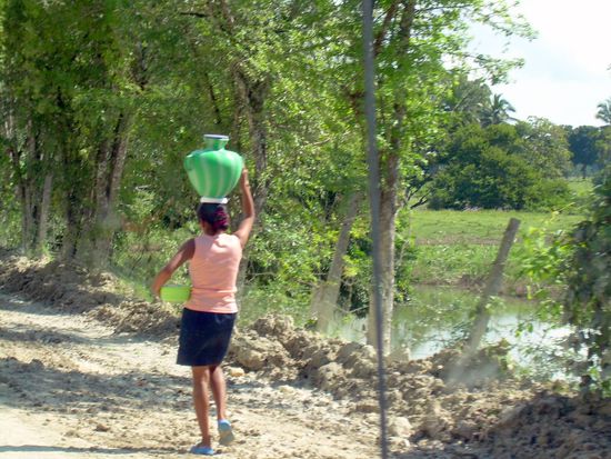 ...Balancing act with a full pitcher over a rough ground-women walk...