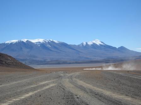 desert, snow-capped mountains and far away some dust from a car
